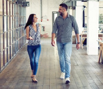 Coworkers chat happily while they walk through an office setting.